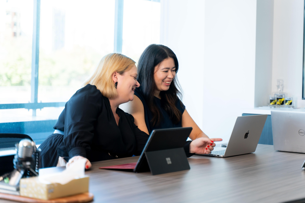 Sarah and Tessa reviewing ChatGPT research on a laptop, discussing insights and strategy.